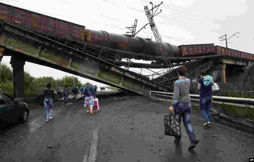 People walk under a destroyed railroad bridge over a main road leading into Donetsk, near the village of Novobakhmutivka, north of Donetsk, eastern Ukraine, July 7, 2014.