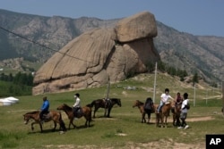 Tourists enjoy horseback riding near the iconic Turtle Rock outcrop at the Terejl National Park outside Ulaanbaatar, Mongolia on July 3, 2024. (AP Photo/Ng Han Guan)