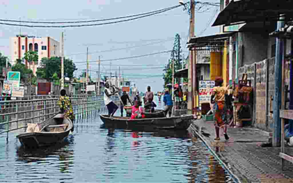 Residents board canoes in a city street flooded by an overflowing drainage canal, in the Saint Martin neighborhood of Cotonou, Benin, 9 Oct 2010