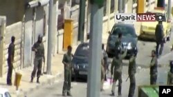 Image made from amateur video released by Ugarit News and accessed via AP TV News on Aug. 8, 2011, shows members of the Syrian military standing near the body of man in the northern Syrian province of Idlib Sunday Aug. 7, 2011. (Contents and date cannot b