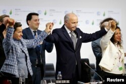 French Foreign Affairs Minister Laurent Fabius (C), President-designate of COP21 and Christiana Figueres (L), Executive Secretary of the UN Framework Convention on Climate Change, hold hands during the final plenary session at the World Climate Change Conference 2015 (COP21) at Le Bourget, near Paris, France, Dec. 12, 2015.