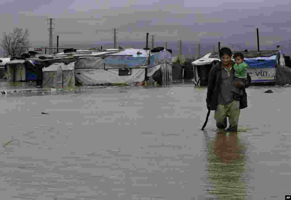 A Syrian refugee man carries his baby as he makes his way through flooded water at a temporary refugee camp, in the eastern Lebanese Town of Al-Faour near the border with Syria, January 8, 2013. 