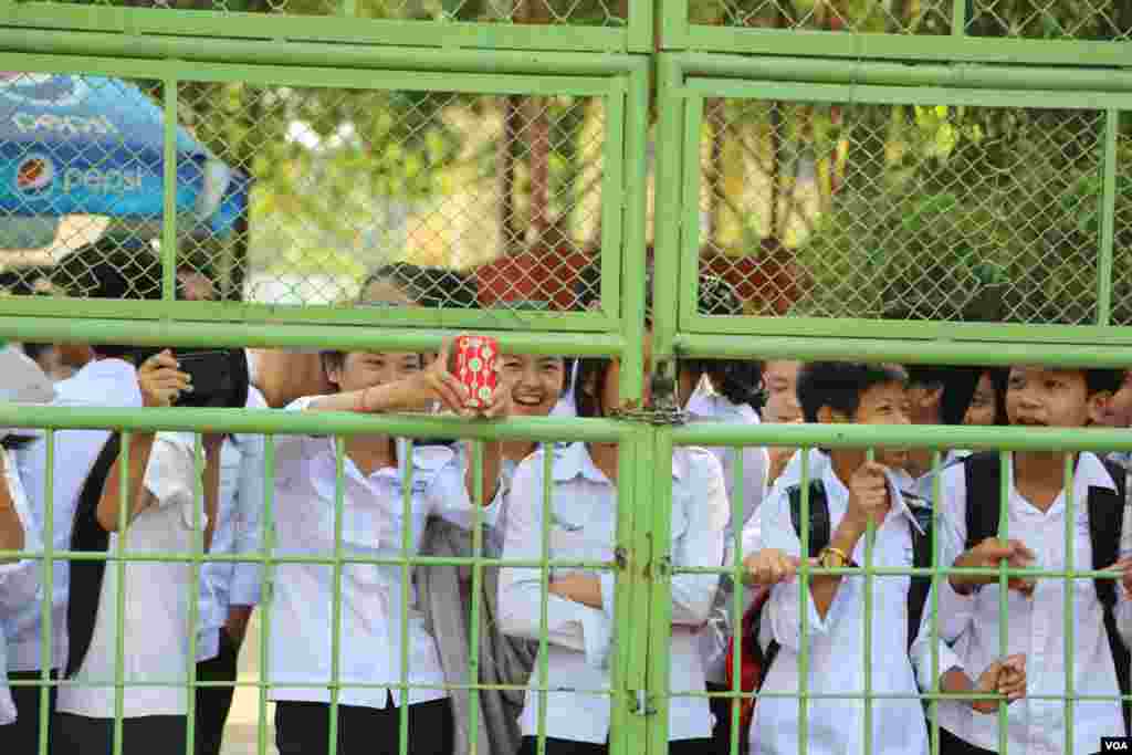 High school students peek through a school gate to cheer and take pictures of a protest in Phnom Penh, Oct. 25, 2013. (Heng Reaksmey/VOA Khmer)