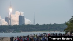 People watch from a beach as the Long March-5B Y2 rocket, carrying the core module of China's space station Tianhe, takes off from Wenchang Space Launch Center in Hainan province, China April 29, 2021.