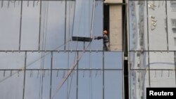 A laborer installs a glass wall on a commercial building under construction in Nanjing, Jiangsu province, China, August 6, 2012.