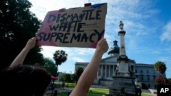 FILE - A demonstrator holds up a sign in front of a civil war statue at the State House in Columbia, South Carolina, July 10, 2020.