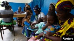 FILE - Women holding children wait for a medical examination at the health center in Gbangbegouine, Ivory Coast.