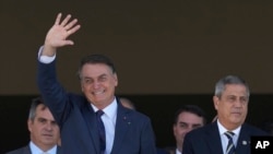 ARCHIVO - El presidente brasileño, Jair Bolsonaro, (Izq) saluda junto a su ministro de Defensa, Walter Braga Netto (Der), mientras un convoy militar pasa por el palacio presidencial de Planalto en Brasilia, Brasil, el 10 de agosto de 2021.