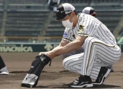 Hanshin Tigers manager Akihiro Yano wearing a face mask puts dirt he collected from the grounds into a bag at Koshien Stadium in Nishinomiya, western Japan, Tuesday, June 16, 2020.