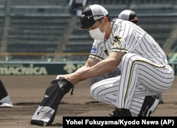 Hanshin Tigers manager Akihiro Yano wearing a face mask puts dirt he collected from the grounds into a bag at Koshien Stadium in Nishinomiya, western Japan, Tuesday, June 16, 2020.