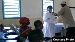 A Red Cross volunteer helps the CDC’s Paulyne Ngalame Ntuba put on personal protective equipment, typically worn by burial teams, in Forecariah, Guinea, on October 5, 2014. (Photo courtesy of Centers for Disease Control and Prevention) 