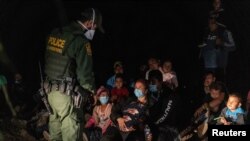 Asylum-seeking migrant families sit on the ground as an U.S. Border Patrol agent checks on them after crossing the Rio Grande river into the United States from Mexico in Roma, Texas, Aug. 14, 2021. 
