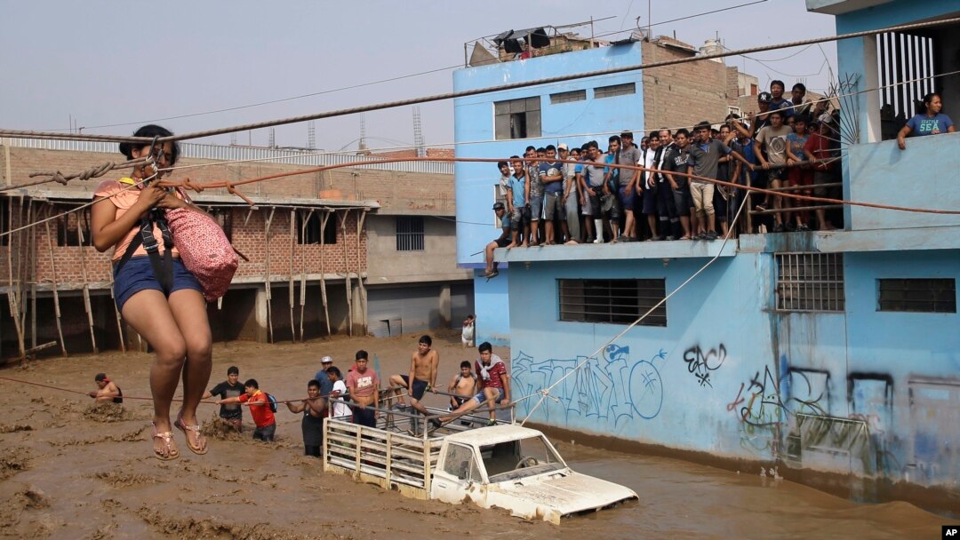 FILE - A woman is pulled to safety in a zip line harness in Lima, Peru, March 17, 2017.