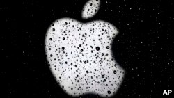 ARSIP – Logo Apple tampak di balik jendela yang diselimuti butir-butir air hujan di luar Apple Store di distrik perbelanjaan Country Club Plaza di Kansas City, 26 Desember 2018 (foto: AP Photo/Charlie Riedel, Arsip)