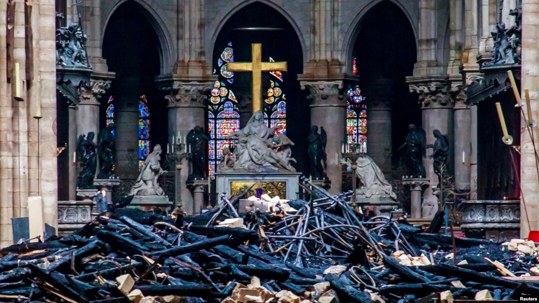 Salib dan patung Pieta oleh Nicolas Coustou tampak di belakang puing-puing setelah kebakaran yang merusak katedral tersebut di Paris, Perancis, 16 April 2019. 