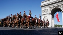 FILE - French Republican Guards ride their horses past the Arc de Triomphe in Paris, July 14, 2017. The annual Bastille Day parade is being opened by American troops with President Donald Trump as the guest of honor.