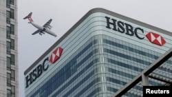 FILE - An aircraft flies past the HSBC headquarters building in the Canary Wharf financial district in east London, Feb. 15, 2015. 