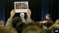 A protester holds up photos of Iranian dissidents under house as Iran's President Hassan Rouhani speaks in New York, Sept. 24, 2014.