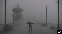 A man struggles against gusty wind and heavy rain as he walks along a pier in Huntington Beach, Calif., Feb. 17, 2017. A major Pacific storm unleashed downpours and fierce gusts on Southern California, triggering flash flood warnings and other problems.