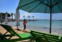 Seorang pria membersihkan pantai di Sanur, Bali yang sepi pengunjung saat penerapan PPKM, 10 Agustus 2021. (Foto: Sonny Tumbelaka/AFP)