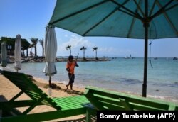 Seorang pria membersihkan pantai di Sanur, Bali yang sepi pengunjung saat penerapan PPKM, 10 Agustus 2021. (Foto: Sonny Tumbelaka/AFP)