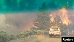 FILE - Flames rise from a treeline near an emergency vehicle during efforts to contain the Spring Fire in Costilla County, Colorado, June 27, 2018. 