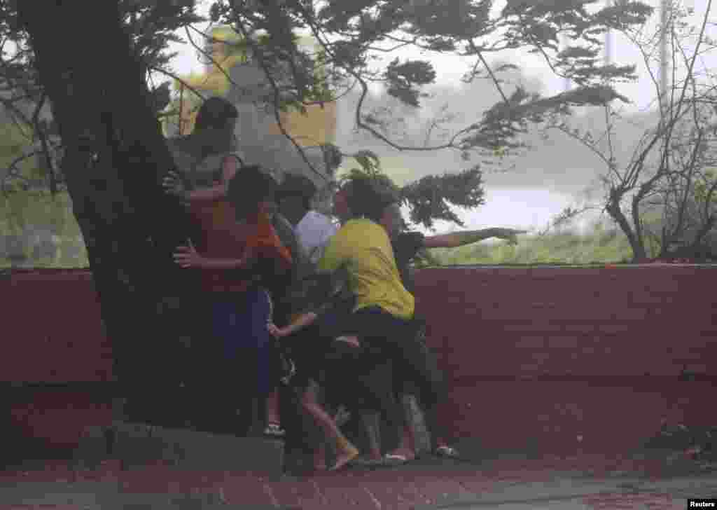 Warga berlindung di bawah pohon setelah angin kencang yang dibawa Topan Rammasun menghantam ibukota Manila (16/7). (Reuters/Romeo Ranoco)
