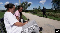 Savannah Brown and Glendy Stollberg use their phone in Kilbourn Reservoir Park Wednesday, Sept. 8, 2021, in Milwaukee. (AP Photo/Morry Gash)