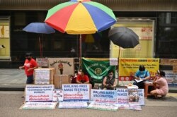 Para pekerja mingran duduk di depan poster yang berisi protes terhadap rencana wajib vaksinasi COVID-19, di distrik Central, Hong Kong, Sabtu, 1 Mei 2021. (Foto: Peter Parks/AFP)