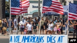 Des gens traversent la rue devant un panneau de protestation contre le système de santé, à Huntington Beach, en Californie, le 19 juillet 2020 au milieu de la pandémie de coronavirus.