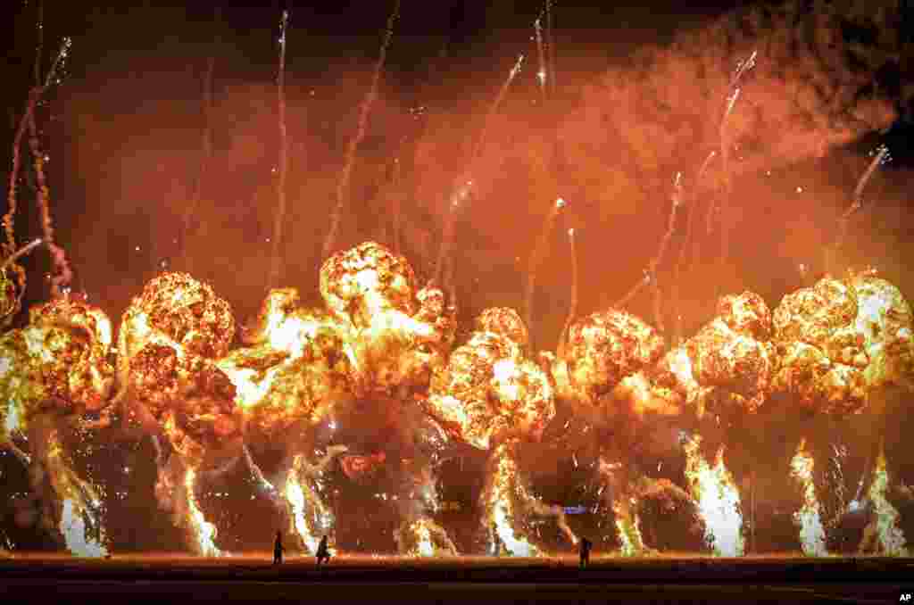 Technicians are backdropped by pyrotechnics going off during an international air show in Bucharest, Romania, Aug. 24, 2019.