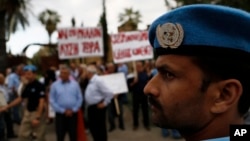 Seorang penjaga perdamaian PBB berjaga-jaga di depan kelompok Yunani dan Turki yang berkumpul di depan hotel tempat perundingan perdamaian berlangsung di Nicosia, Siprus (11/5). (AP/Petros Karadjias)