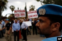 FILE - A U.N. peacekeeper stands guard in front of Greek and Turkish Cypriots as they gather outside the Ledra Palace Hotel, Nicosia, Cyprus, May 11, 2015.