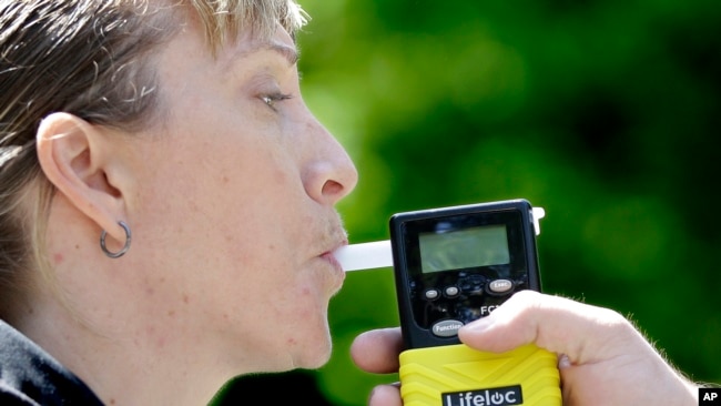 California Highway Patrol Sgt. Jaimi Kenyon blows into a breathalyzer held by Sacramento Police Corporal Luke Moseley during a demonstration of devices <a href=