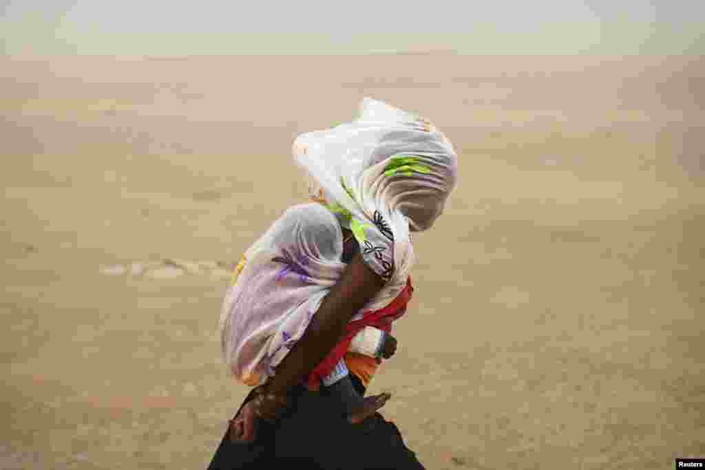 A woman carrying her baby and wrapped with a shawl walks through a sandstorm in Timbuktu, Mali, July 29, 2013. 