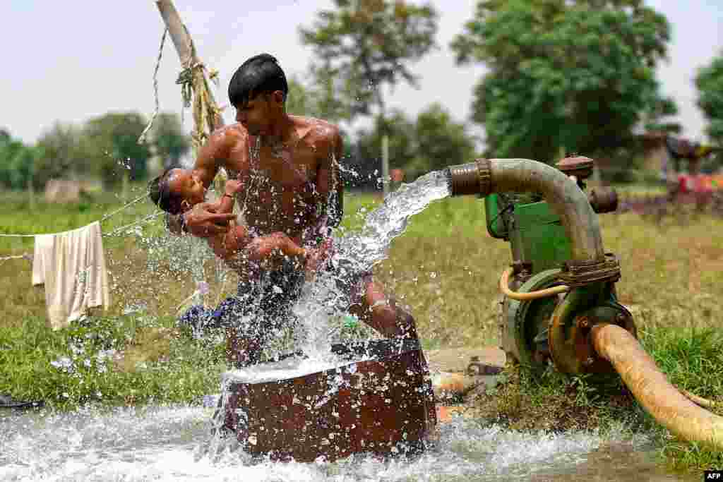 A man gives his son a bath using a water tube well near a field, as the temperature rises in New Delhi, India.