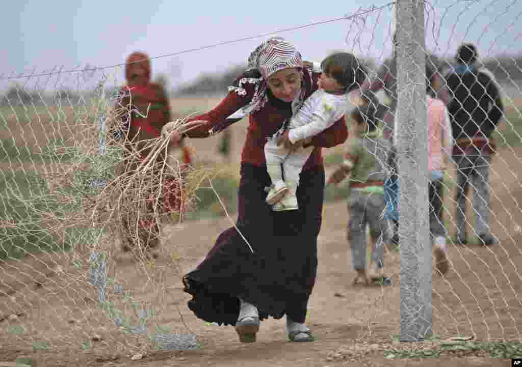 Une réfugiée kurde syrienne de Kobané, un bébé en main, recueille des branches pour allumer un feu dans un camp de réfugiés dans Suruc, près de la frontière Turquie-Syrie, jeudi 23 octobre 2014.