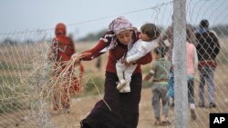 Seorang pengungsi Suriah menggendong bayi sambil membawa ranting yang dikumppulkannya untuk menyalakan api di sebuah lokasi pernampungan pengungsi di Suruc, dekat perbatasan Turki dan Suriah (Foto: dok). 