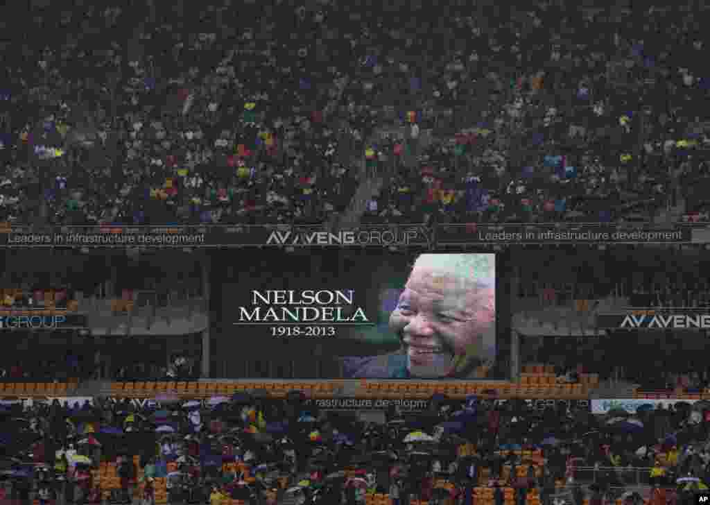 Spectators shelter under umbrellas as the rain lashes down during the memorial service for former South African president Nelson Mandela at the FNB Stadium in Soweto, near Johannesburg, South Africa, Dec. 10, 2013.