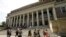 FILE - People walk past an entrance to Widener Library, behind, on the campus of Harvard University, in Cambridge, Massachusetts, July 16, 2019.