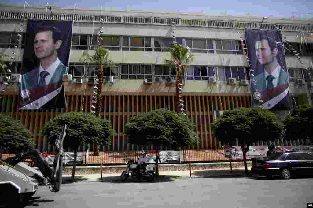 A traffic police officer rests in front of a building with posters of Syrian President Bashar al-Assad in Damascus, June 3, 2014.