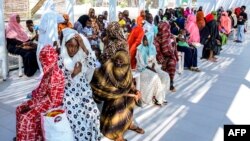 (FILE) Women with children wait in the shade to receive medical care outside the Italian Paediatric Hospital in Port Sudan on October 8, 2024.