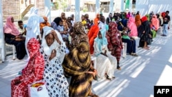 FILE - Women with children wait in the shade to receive medical care outside the Italian Paediatric Hospital in Port Sudan on Oct. 8, 2024.