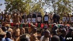 Des responsables militaires se tiennent sur un camion dans la section militaire du cimetière de Gounghin à Ouagadougou le 23 novembre 2021 avec les cercueils et des photos de soldats burkinabés tués lors de l'attaque d'un camp de gendarmerie à Inata le 14 novembre 2021.