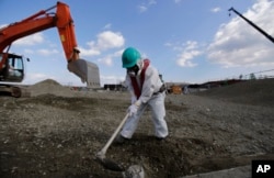 FILE - A worker, wearing a protective suit and a mask, levels ground at the tsunami-crippled Fukushima Dai-ichi nuclear power plant, operated by Tokyo Electric Power Co. (TEPCO), in Okuma, Fukushima Prefecture, northeastern Japan, Feb. 10, 2016.