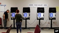 FILE - An investigator with the Georgia Secretary of State office, left, takes a look at a new voting machine that produces a paper record being tested at a polling site in Conyers, Ga., Oct. 19, 2017.