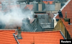 A masked Belgian policeman secures the area from a rooftop above the scene where shots were fired during a police search of a house in the suburb of Forest near Brussels, March 15, 2016. Teargas is seen at left.