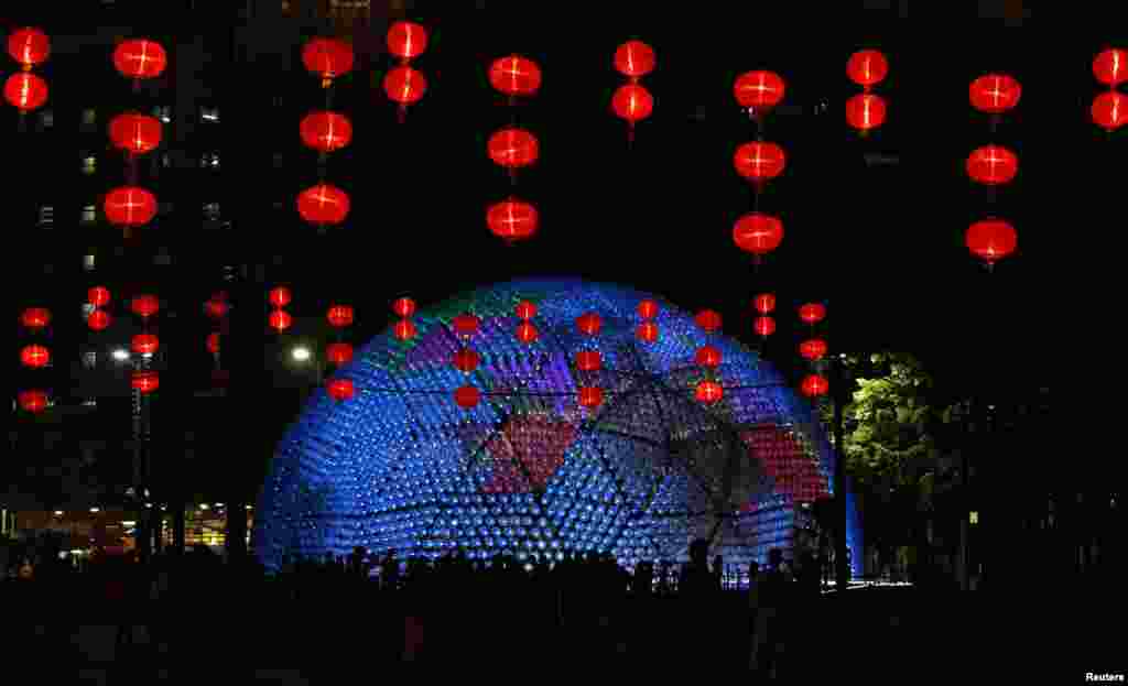 The &quot;Rising Moon&quot;, a giant lantern, containing 7,000 recycled plastic water bottles with LED lights, measuring 20 meters in diameter and 10 meters in height, shines behind traditional Chinese lanterns at Hong Kong&#39;s Victoria Park.