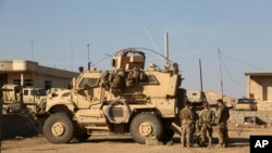 FILE - U.S. soldiers stand outside their armored vehicle on a joint base with Iraqi army south of Mosul, Iraq, Feb. 23, 2017.