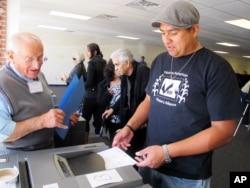 FILE - In this Oct. 26, 2012, photo, Dashiell Beardsley, right, feeds his ballot into a voting machine during early voting in Albuquerque, N.M.